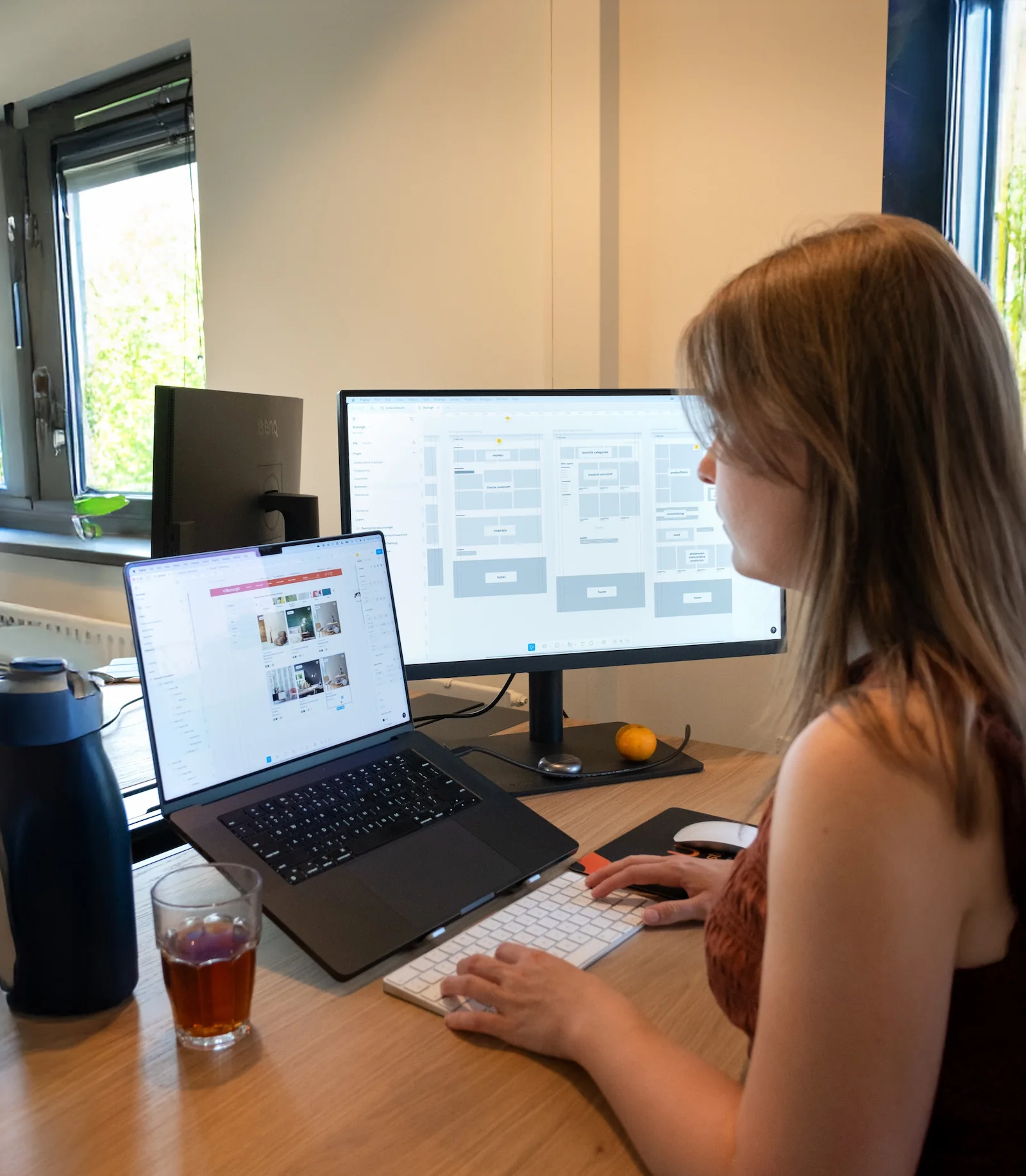 Vrouw werkt aan webdesign op laptop en extern scherm in een modern kantoor.