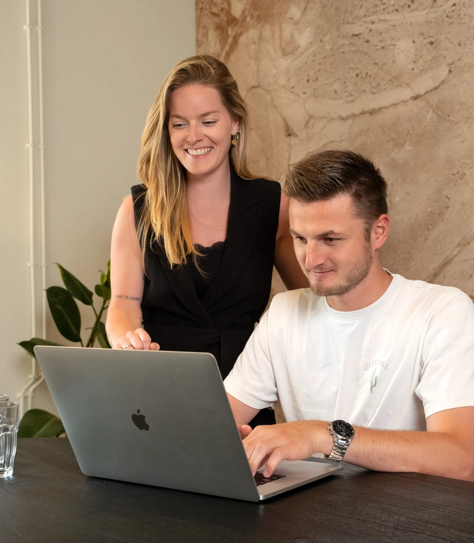 Twee collega’s werken samen aan website-hosting op een laptop aan een bureau.